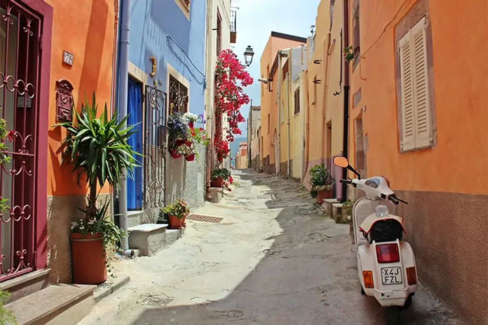 Smal gränd med färgglada fasader, blommor och en parkerad vespa